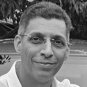 Portrait of a middle-aged man wearing glasses smiling slightly with trees in the background.