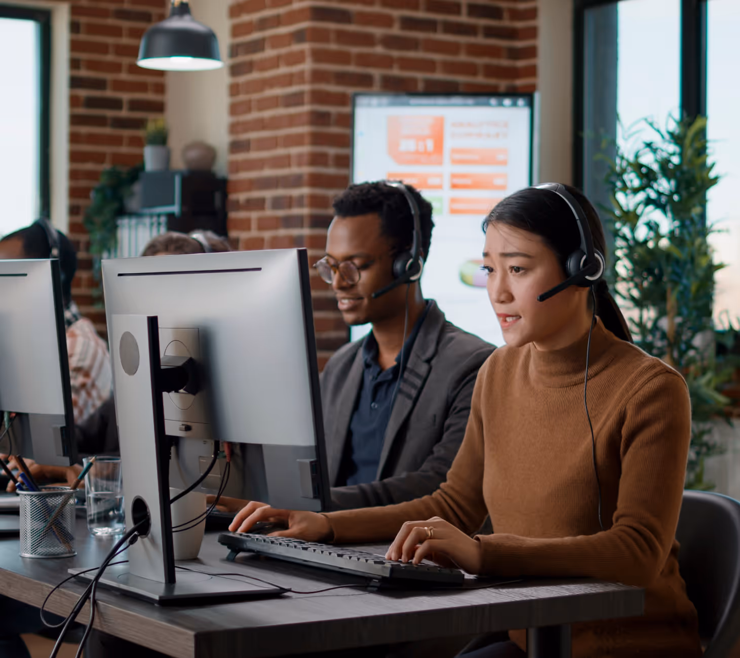 Two customer service representatives wearing headsets working at computers in a modern office.