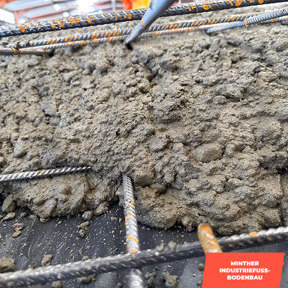 Frisch gegossener Beton mit sichtbaren Stahlbewehrungsstäben auf einer Baustelle.