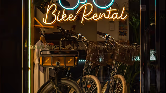 Bicycles parked inside a bike rental shop with an illuminated neon sign reading 'Bike Rental' above them.