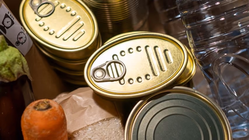 Stack of canned goods, plastic water bottle, carrot, and bag of rice on a surface.