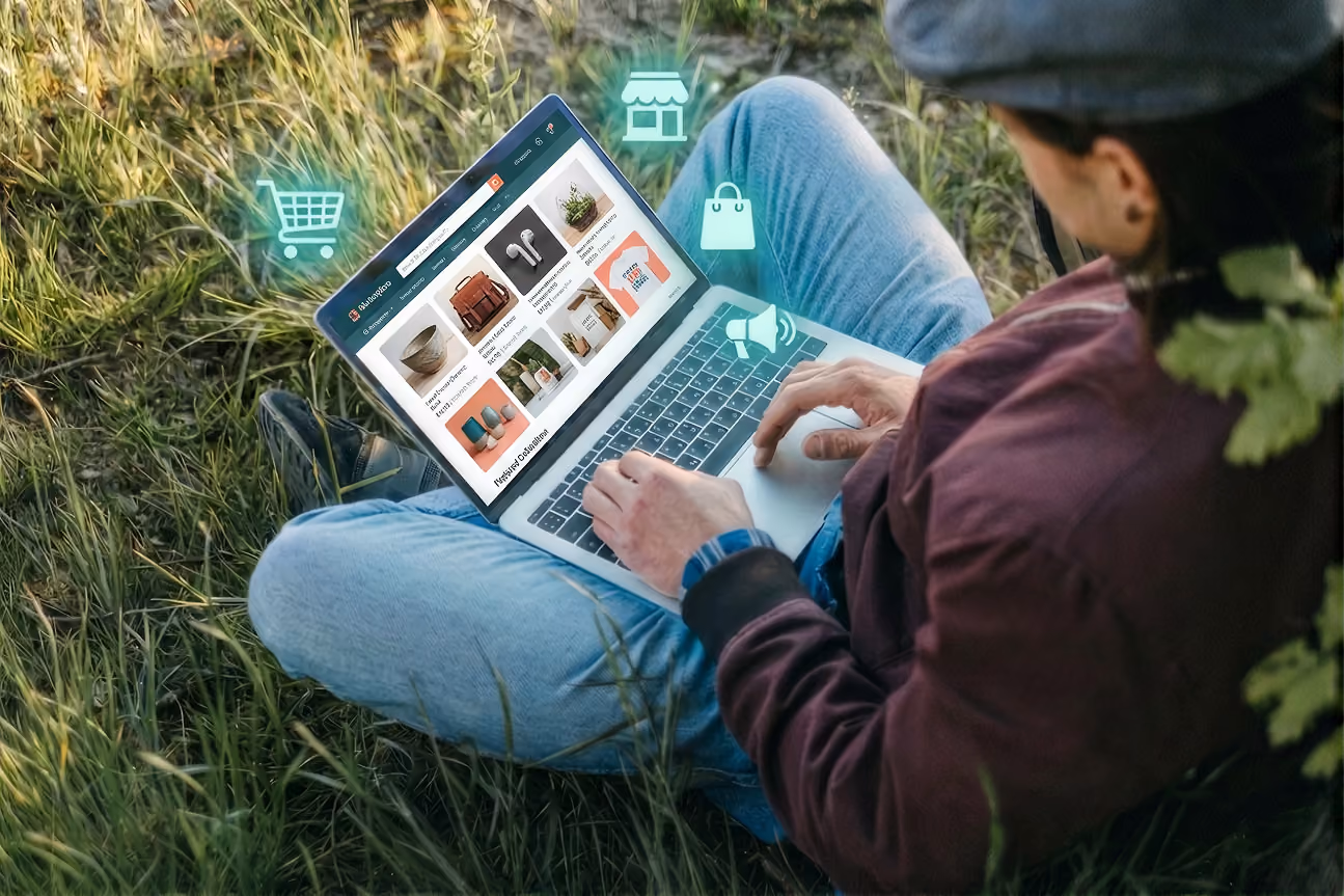 A persons sitting on grass, using macbook, browsing on online marketplace for his item