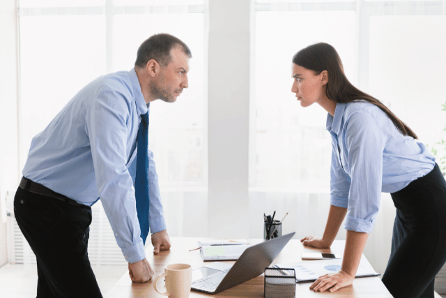 Dos personas discuten en una oficina, frente a frente, en un ambiente de tensión laboral.