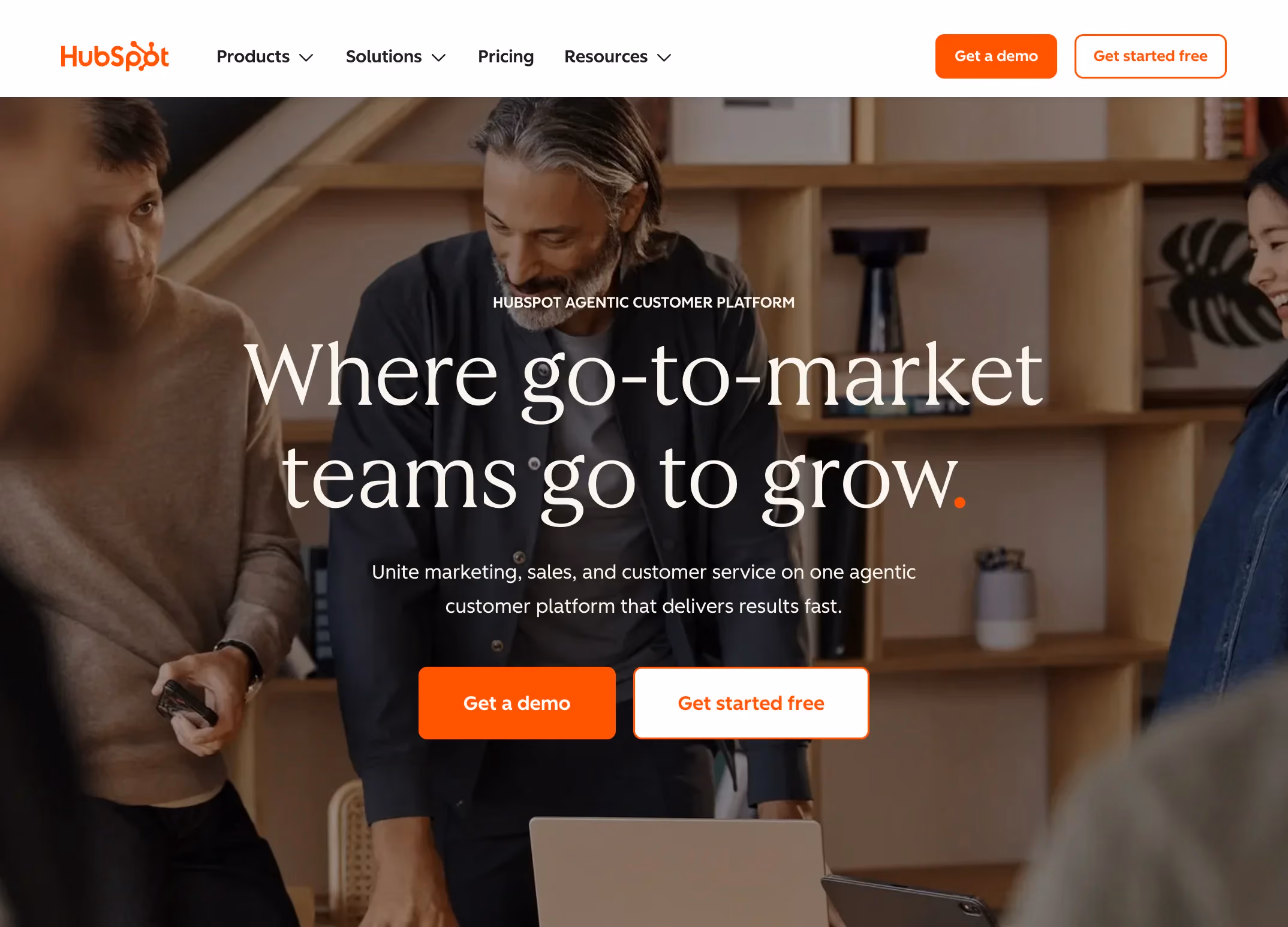 HubSpot homepage hero section with a dark background image of three people collaborating, featuring the headline "Where go-to-market teams go to grow" and two call-to-action buttons, "Get a demo" and "Get started free."