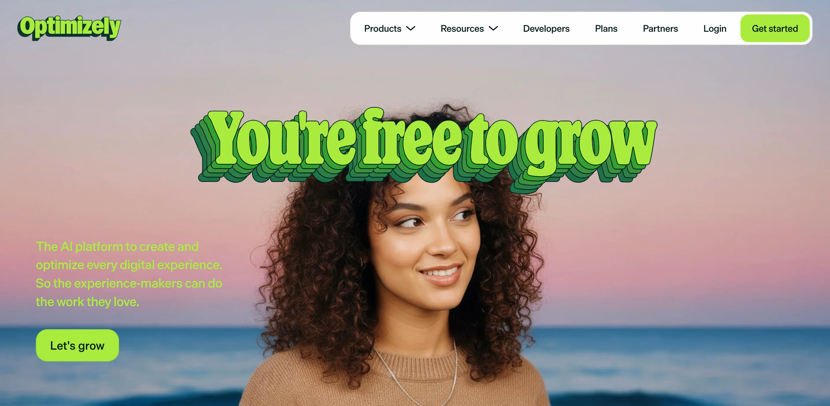 Optimizely website homepage with the headline "you're free to grow" in green retro-style lettering placed above a smiling woman with curly hair against a sunset beach background. Below the headline is text about the AI platform to create and optimize digital experiences, with a "let's grow" call-to-action button.