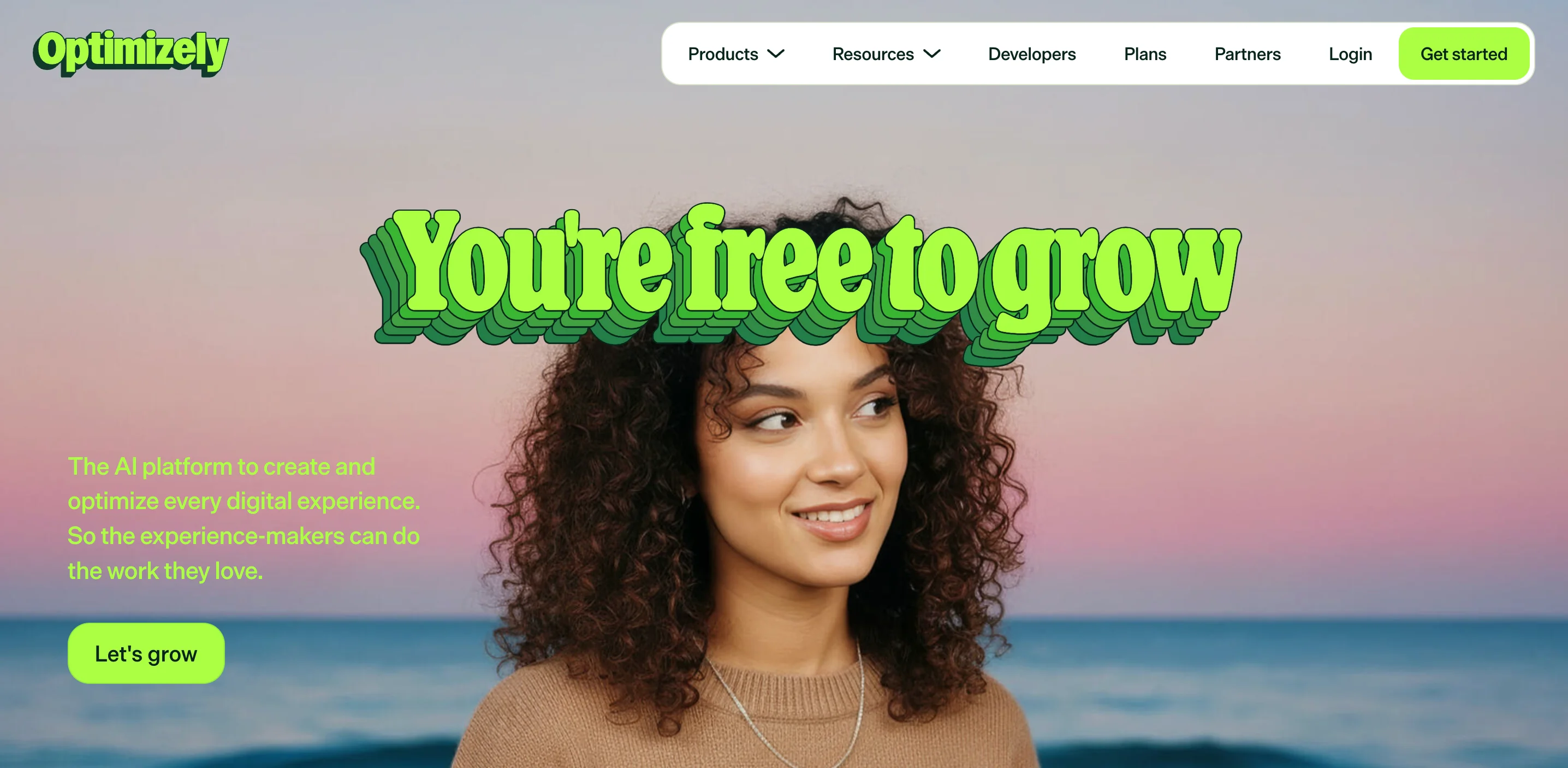 Optimizely website homepage with the headline "you're free to grow" in green retro-style lettering placed above a smiling woman with curly hair against a sunset beach background. Below the headline is text about the AI platform to create and optimize digital experiences, with a "let's grow" call-to-action button.