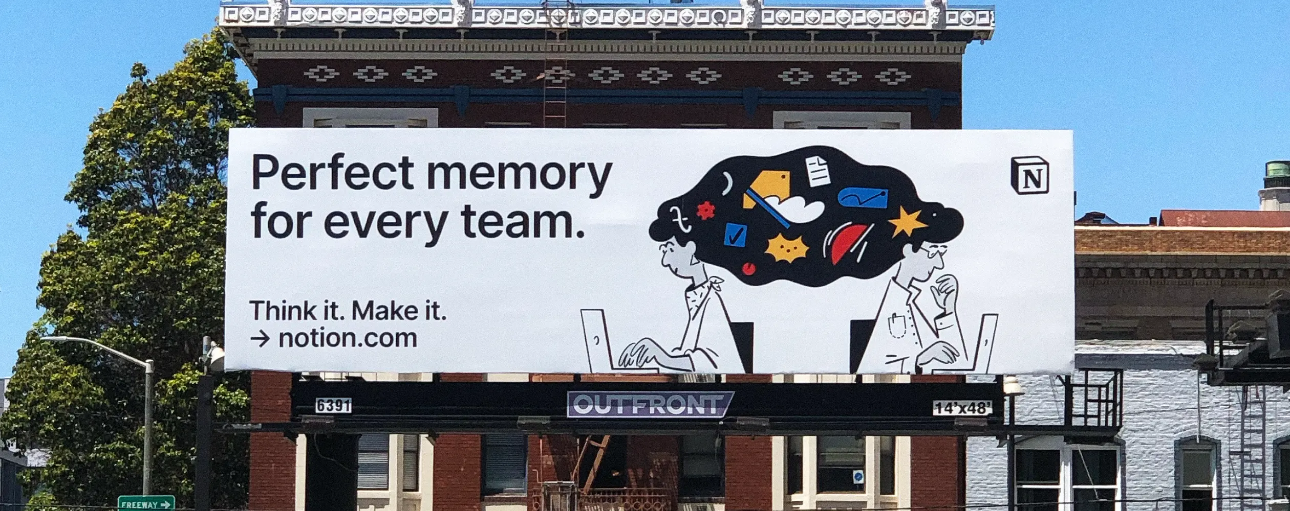 A black-and-white outdoor billboard for Notion reading "Perfect memory for every team," showing two illustrated people at laptops with a cloud of colorful icons above their heads.