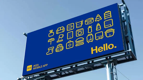 A blue IKEA billboard reading "Hello." next to a grid of simple yellow line icons representing home goods, promoting the IKEA mobile app.