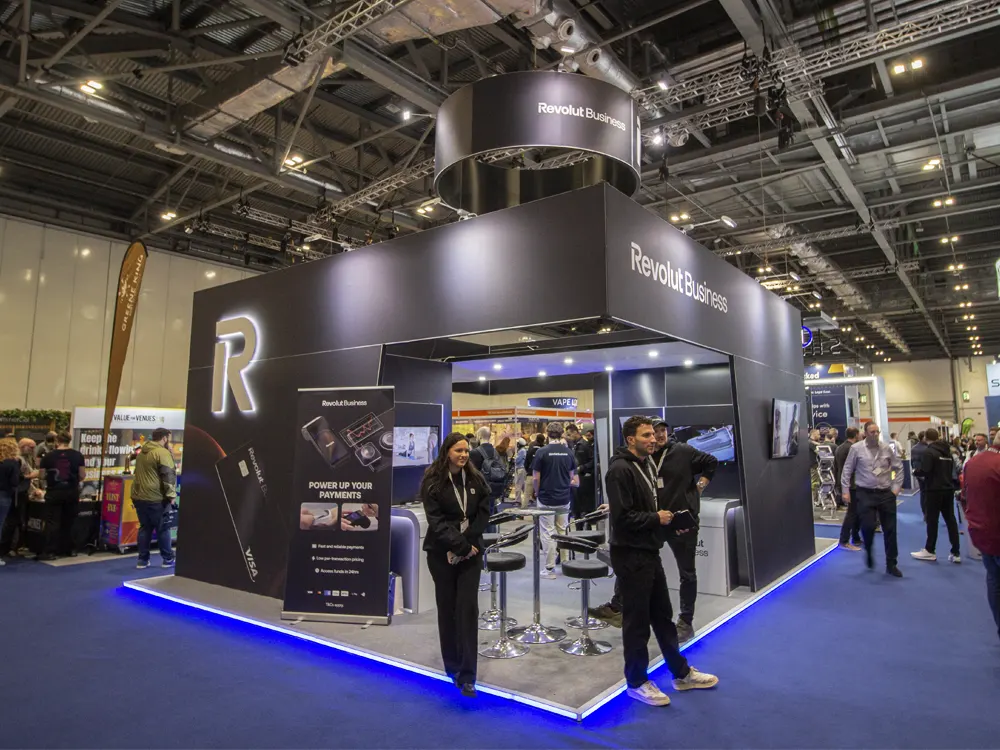 Revolut Business trade show booth with black walls, a lit R logo, an overhead ring sign, and blue LED edge lighting
