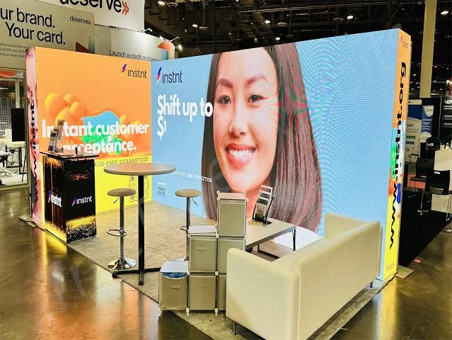 Instnt trade show booth with a large LED wall showing a smiling woman and an orange panel reading Instant customer acceptance
