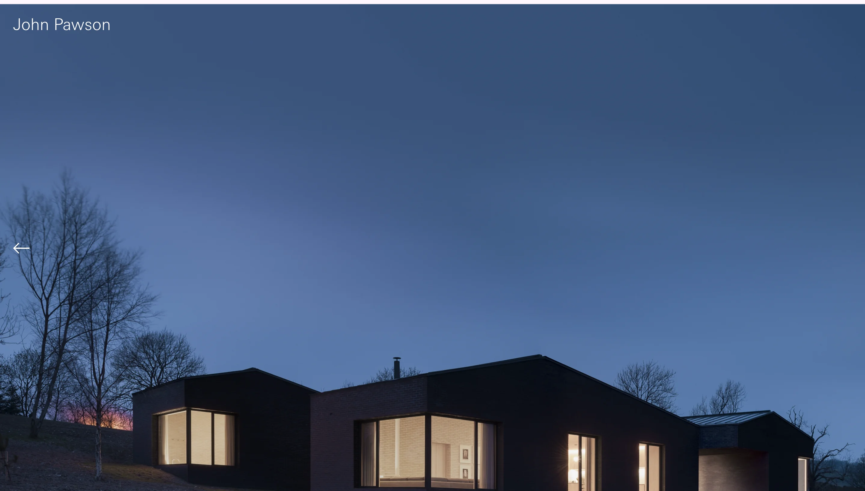 John Pawson homepage hero showing a dark brick house with lit windows at dusk under a deep blue sky