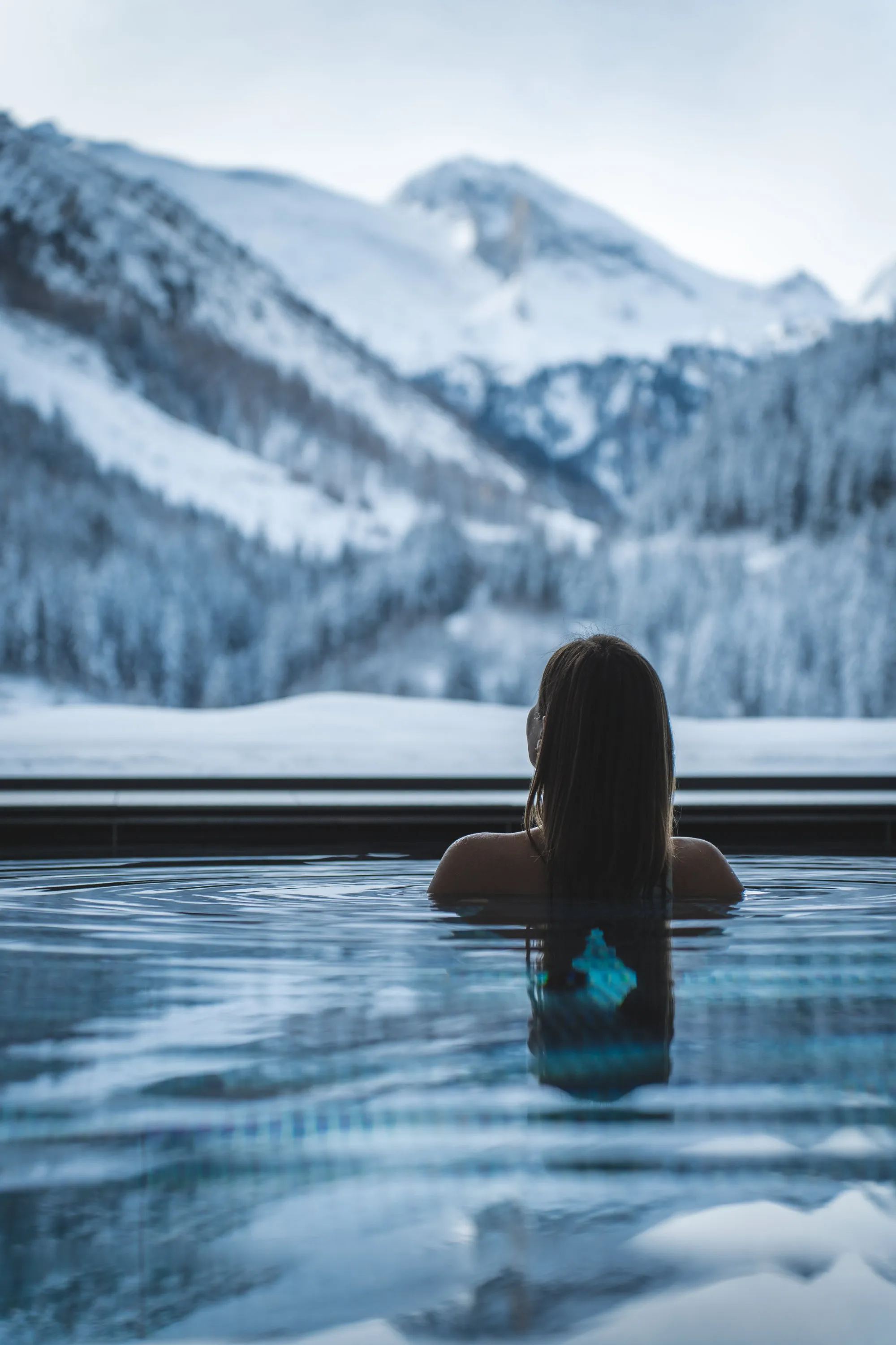 Frau entspannt sich im Pool mit Blick auf schneebedeckte Berge und Wald.