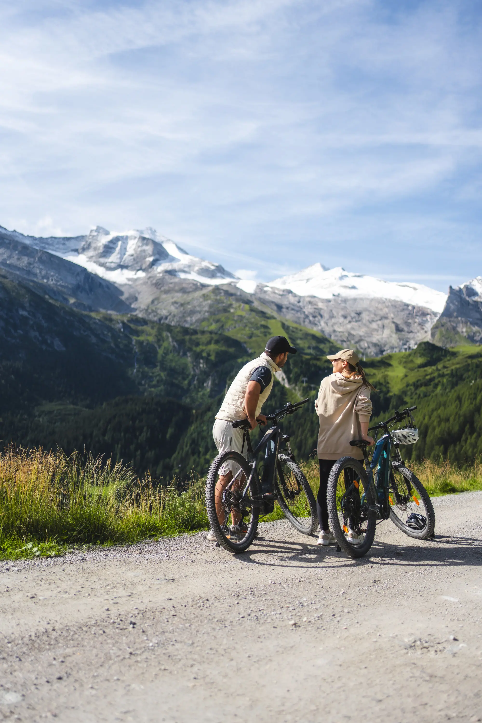 Paar mit E-Bikes auf einer Schotterstraße, dahinter vergletscherte Gipfel.