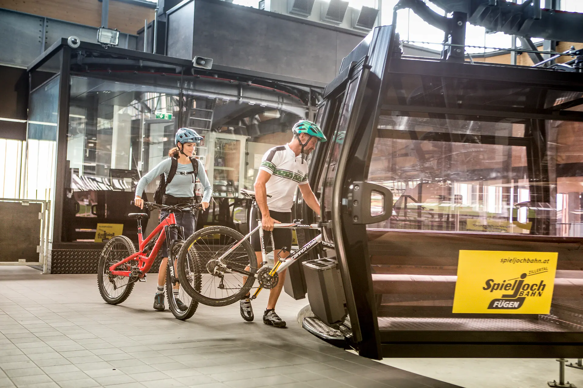 Zwei Mountainbiker schieben ihre Räder in die Kabine einer Bergbahn.