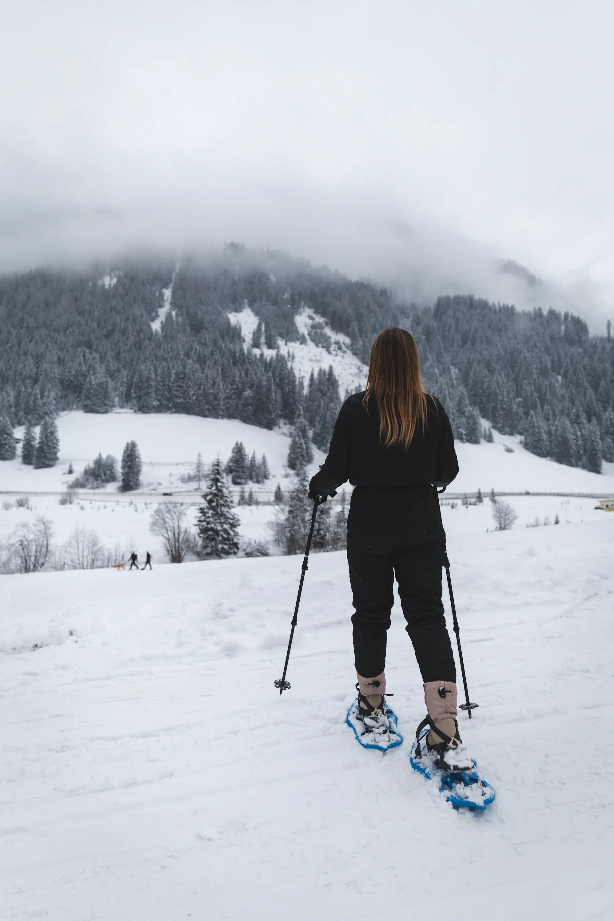 Frau mit Schneeschuhen unterwegs im tief verschneiten Wald.