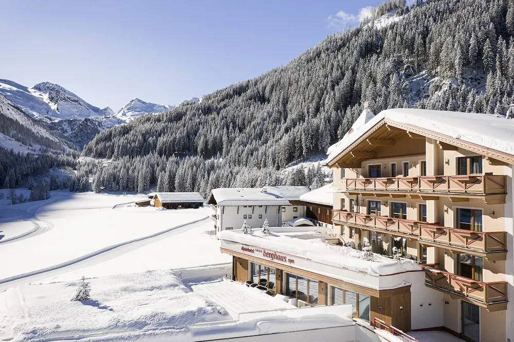 Alpinhotel Berghaus im Schnee bei Sonne vor der Bergkulisse des Tuxertals.