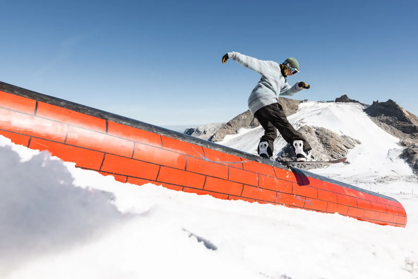 Snowboarder auf einer Rail im Funpark bei blauem Himmel.