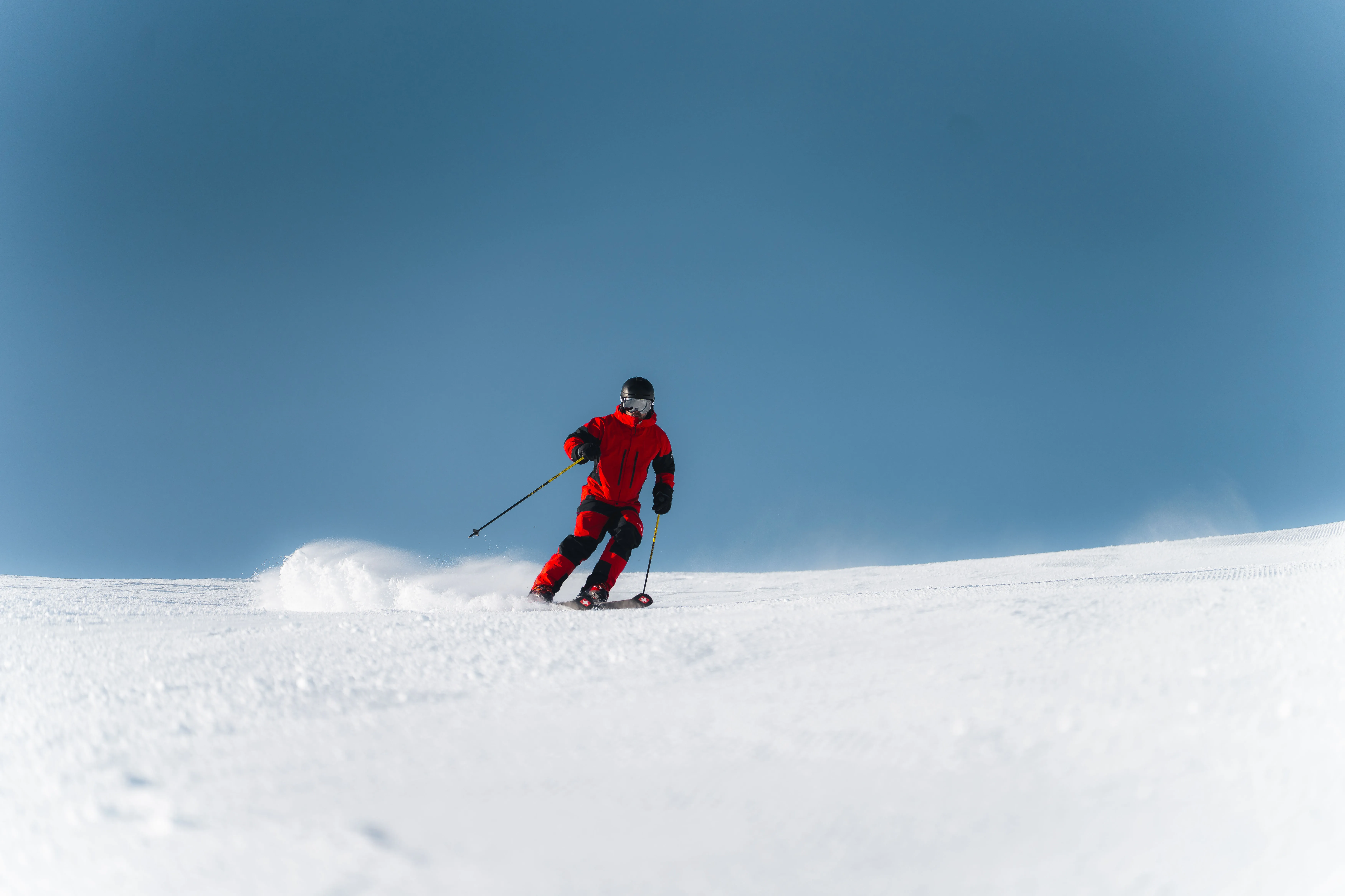 Skifahrer in der Kurve auf einer sonnigen Piste vor blauem Himmel.