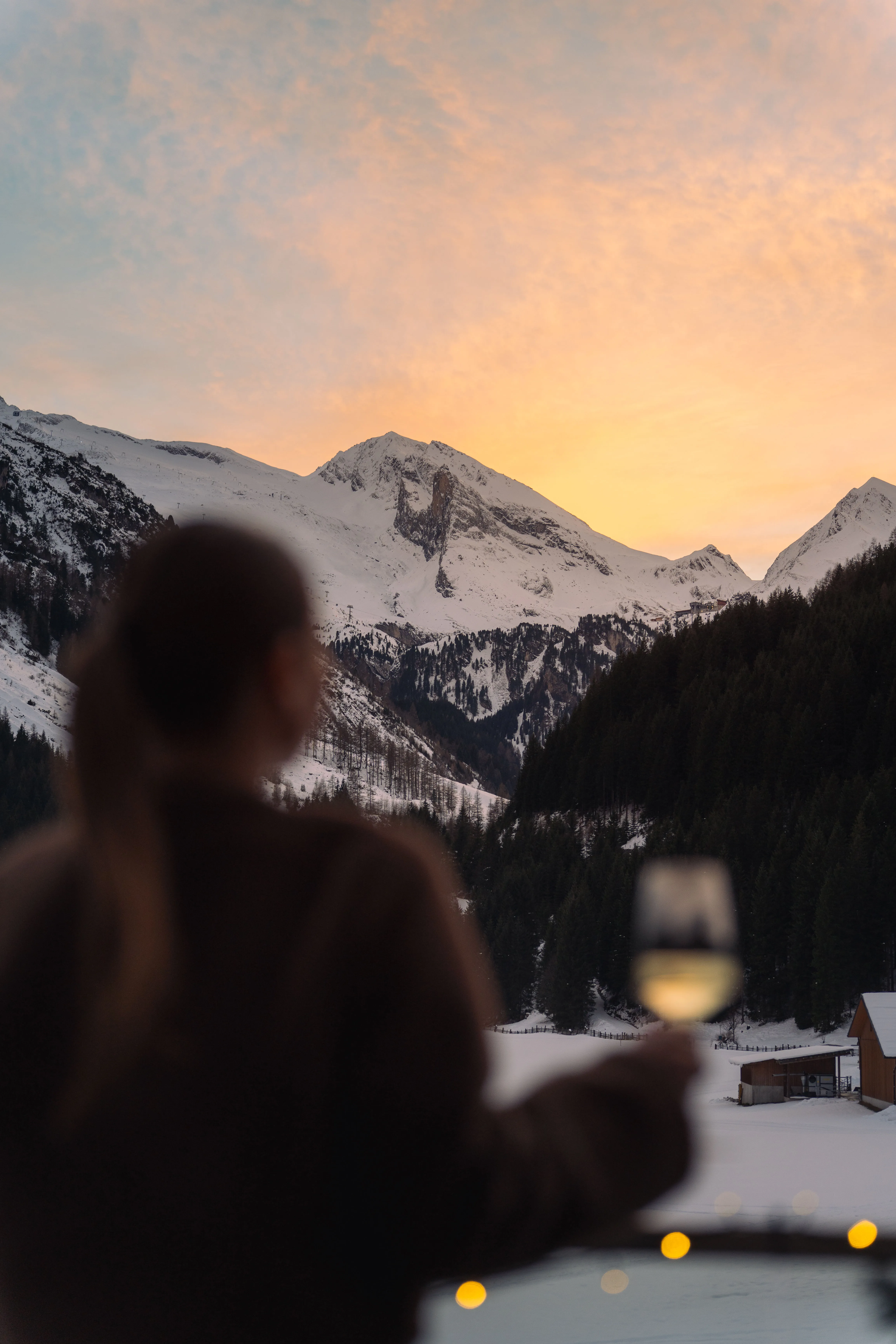 Hotelgast mit einem Glas auf der Terrasse, davor das verschneite Tuxertal im Abendlicht.