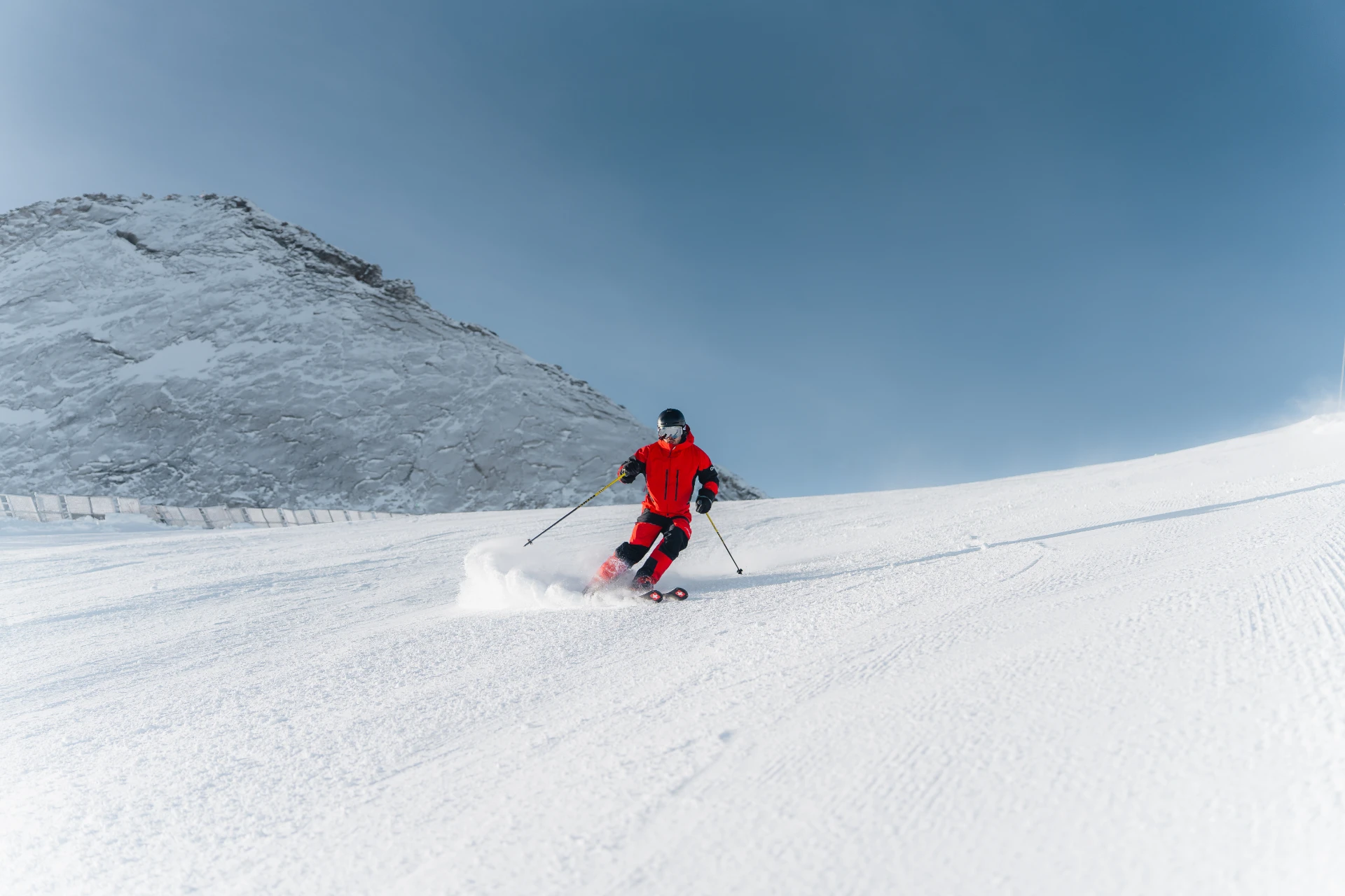 Skifahrer im Schwung auf einer frisch präparierten Piste bei blauem Himmel.