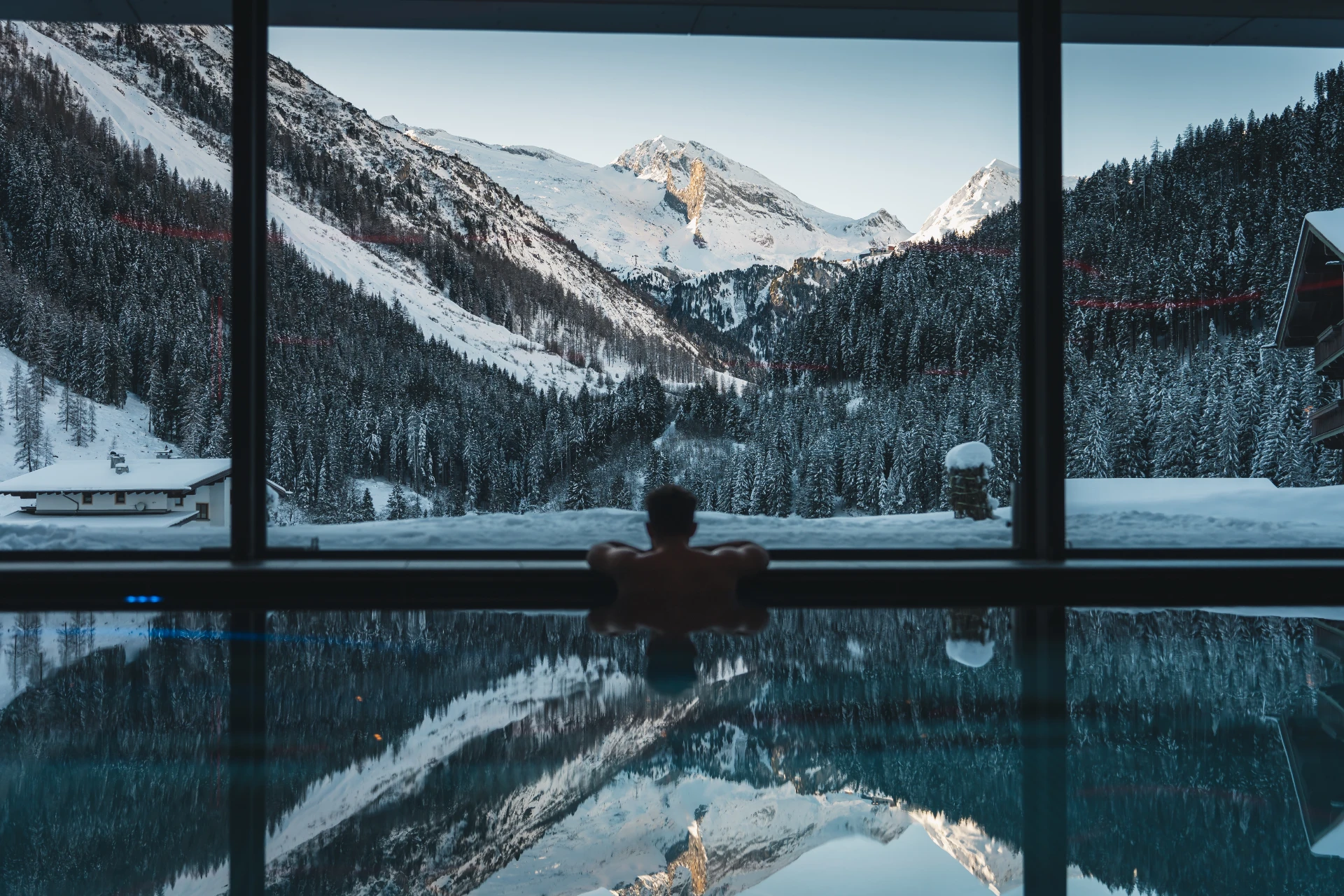 Gast im Panoramahallenbad mit Blick auf die verschneiten Berge des Tuxertals.