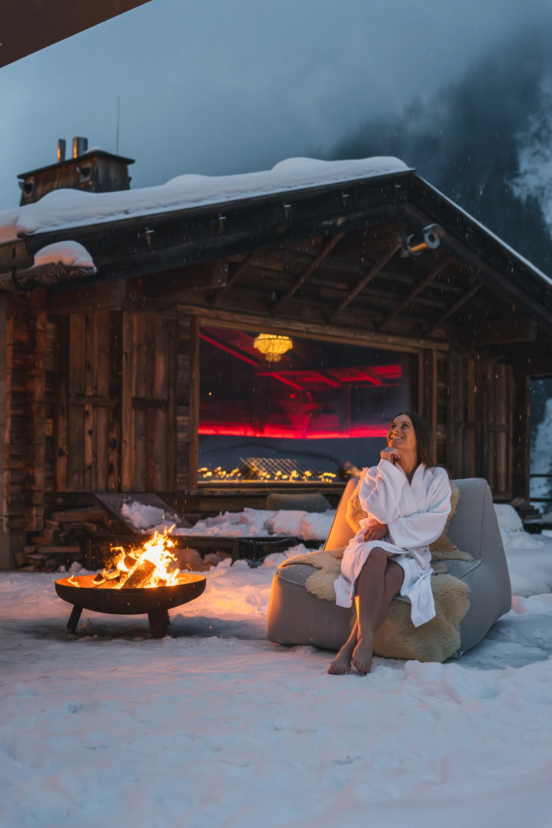 Hotelgast im Bademantel vor dem Saunahaus mit Feuerschale im Schnee.