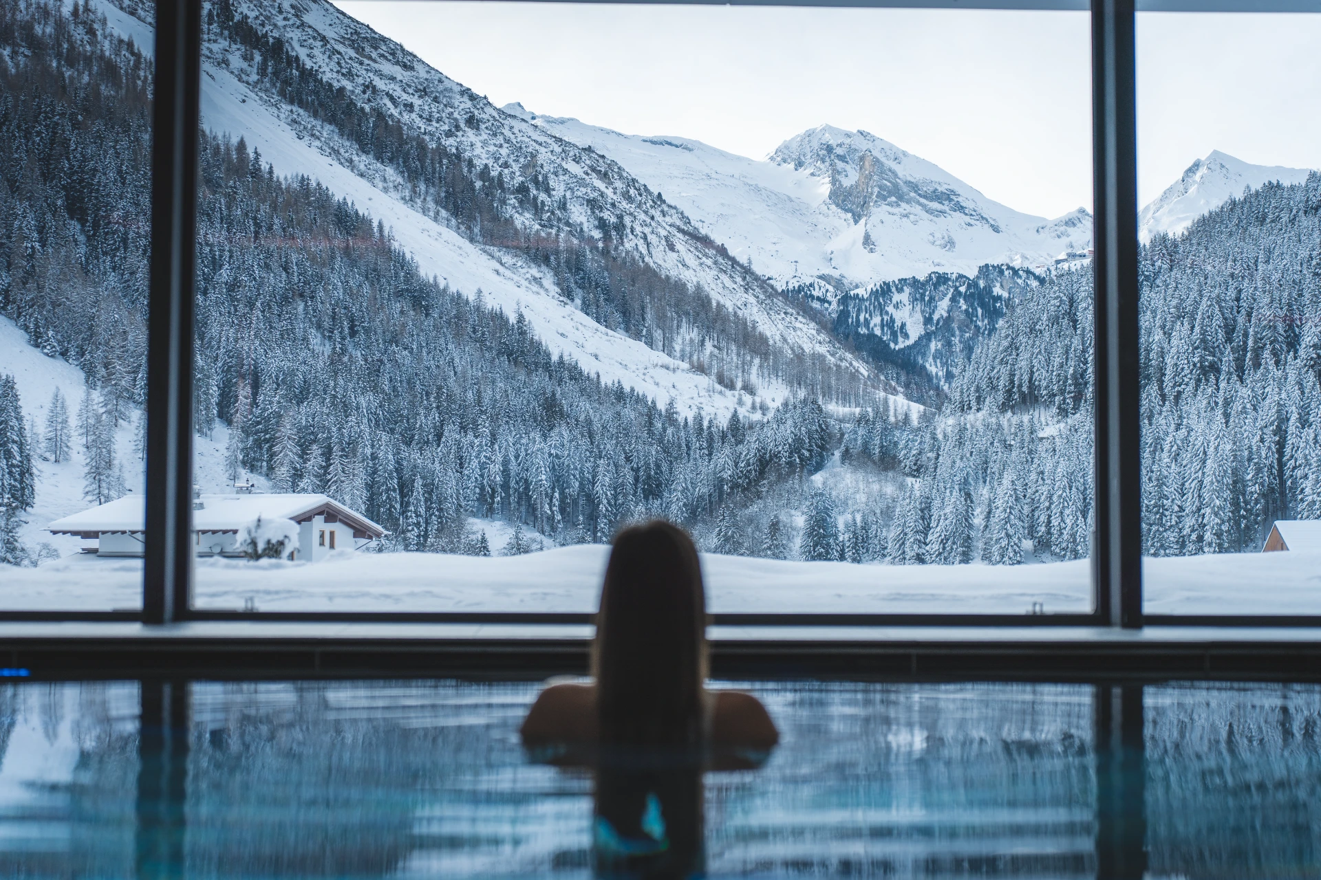 Hotelgast im Panoramahallenbad mit Blick auf das verschneite Tuxertal.