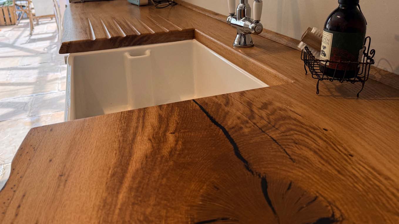 Close-up of bespoke wooden kitchen worktop with built-in white sink and chrome faucet.