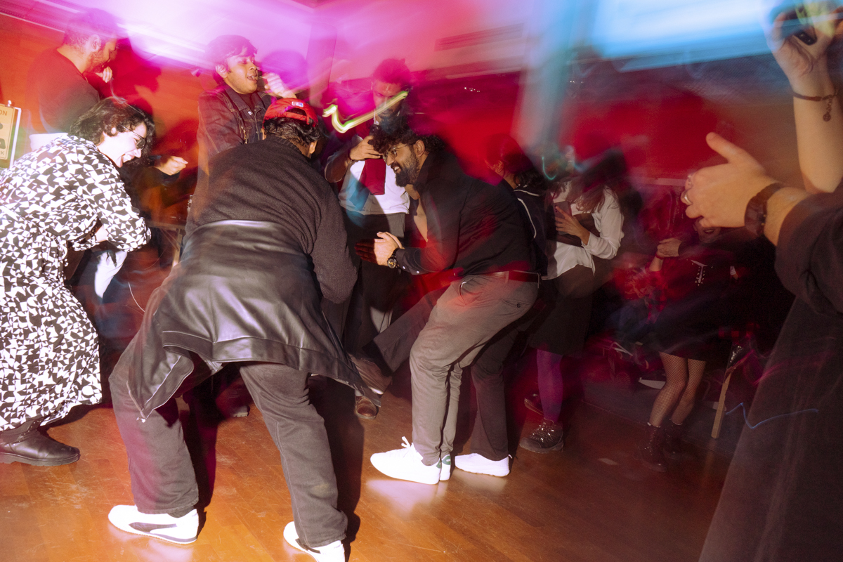 A lively group of people dancing indoors with colorful red and blue lighting, blurred motion capturing movement and energy.