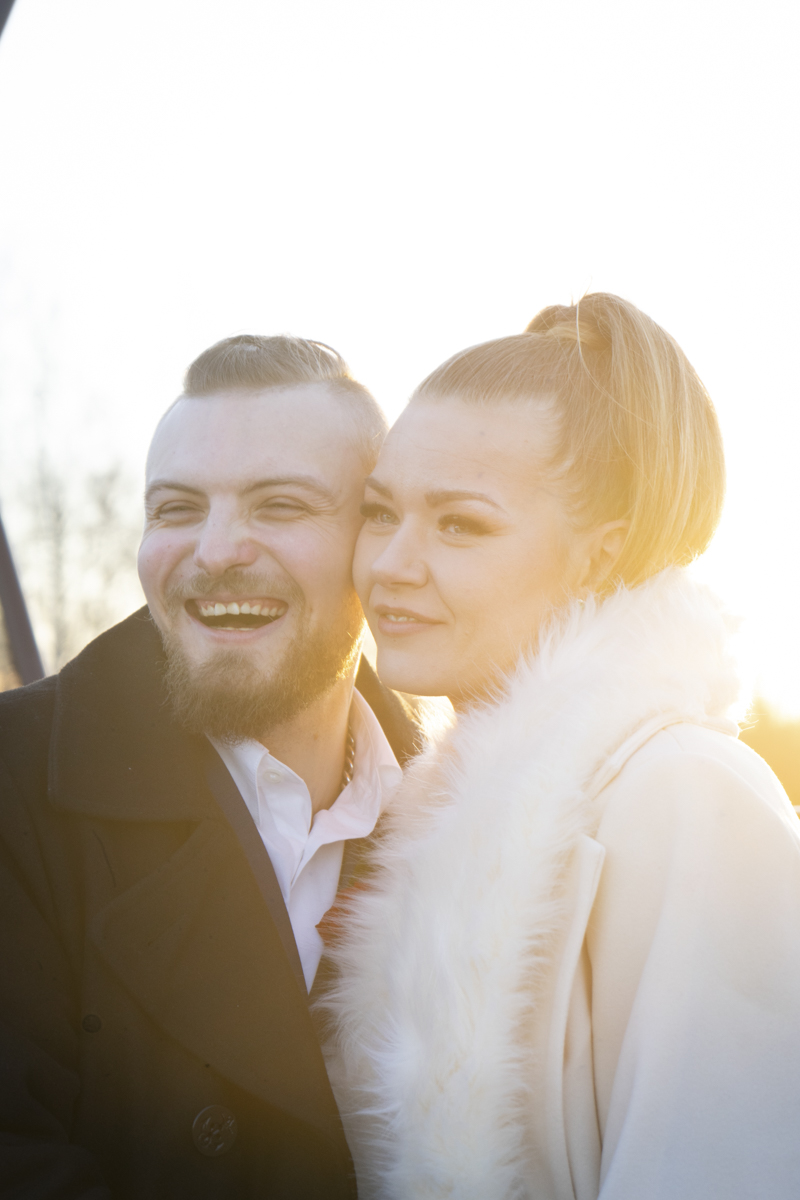 Smiling couple close together outdoors with warm sunlight highlighting them from behind.