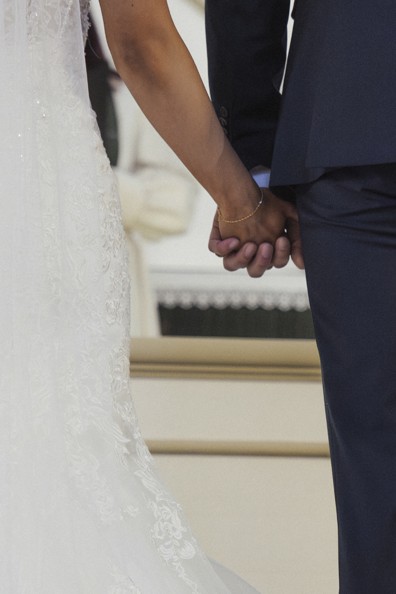 Close-up of a couple holding hands, the bride wearing a white lace wedding dress and the groom in a dark suit.