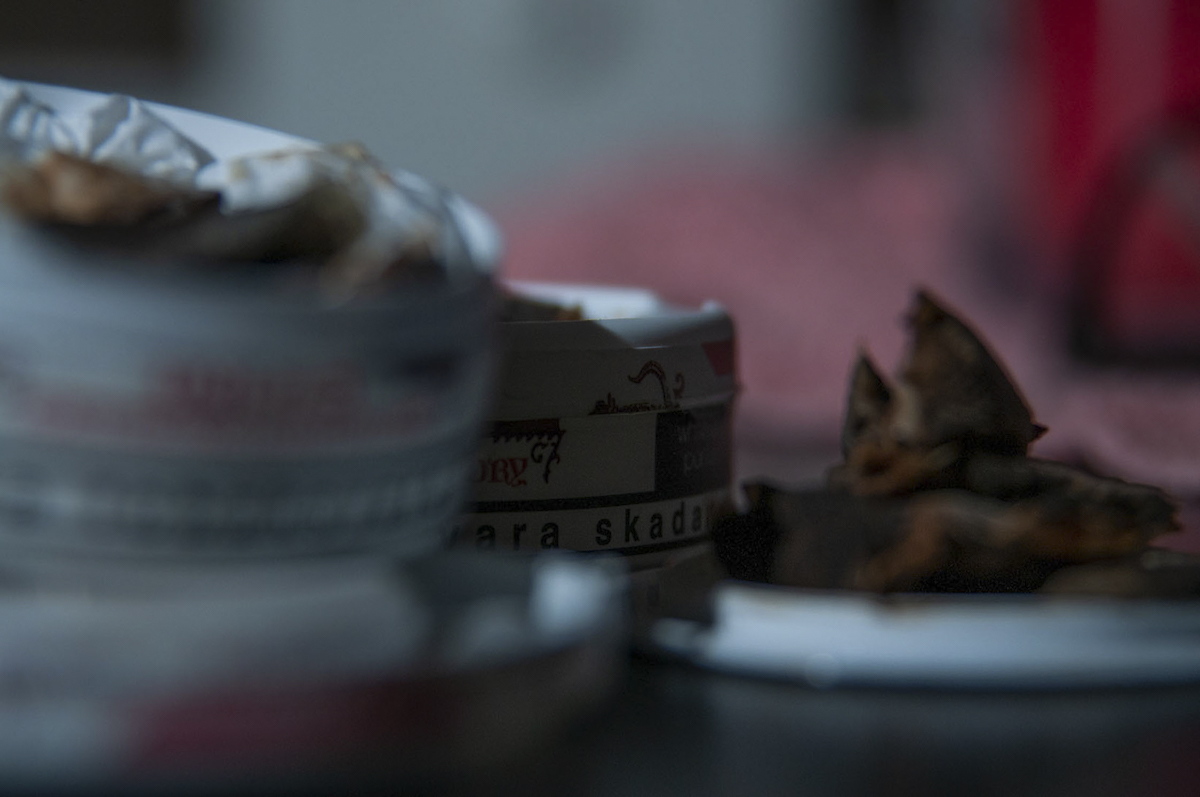 Close-up of partially opened tin containers with tobacco and cigarette butts on a surface in dim lighting.