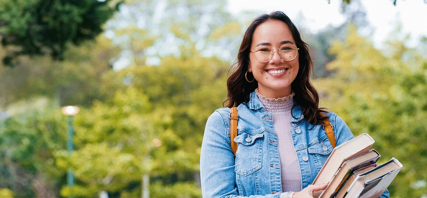 CBS Scholarships — A student outside with books in her hands.