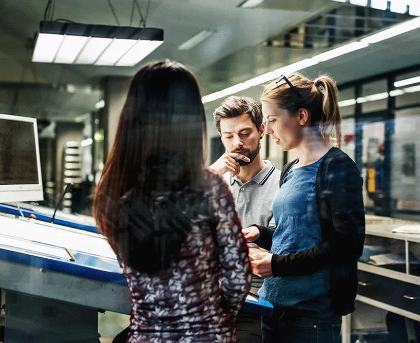 Duales Studium an der CBS: Drei Studierende diskutieren ein Projekt in einem modernen Arbeitsumfeld. Praxisnahe Ausbildung mit direktem Unternehmensbezug.