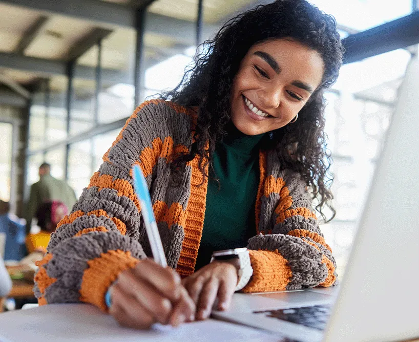 Vollzeit Studium an der CBS: Glückliche Studentin lernt in einer modernen Umgebung mit Laptop und Notizbuch – praxisnahe Hochschulausbildung mit flexiblen Lernmöglichkeiten.