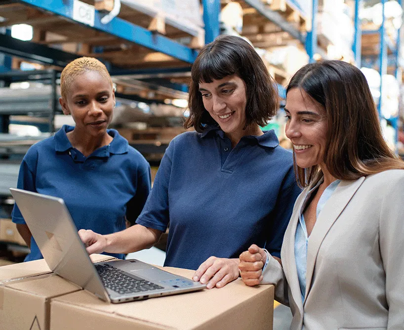 Berufsbegleitendes Studium an der CBS: Drei Frauen in einer Lagerhalle besprechen eine Aufgabe am Laptop – praxisnahe Weiterbildung neben dem Beruf für Karriereaufstieg.