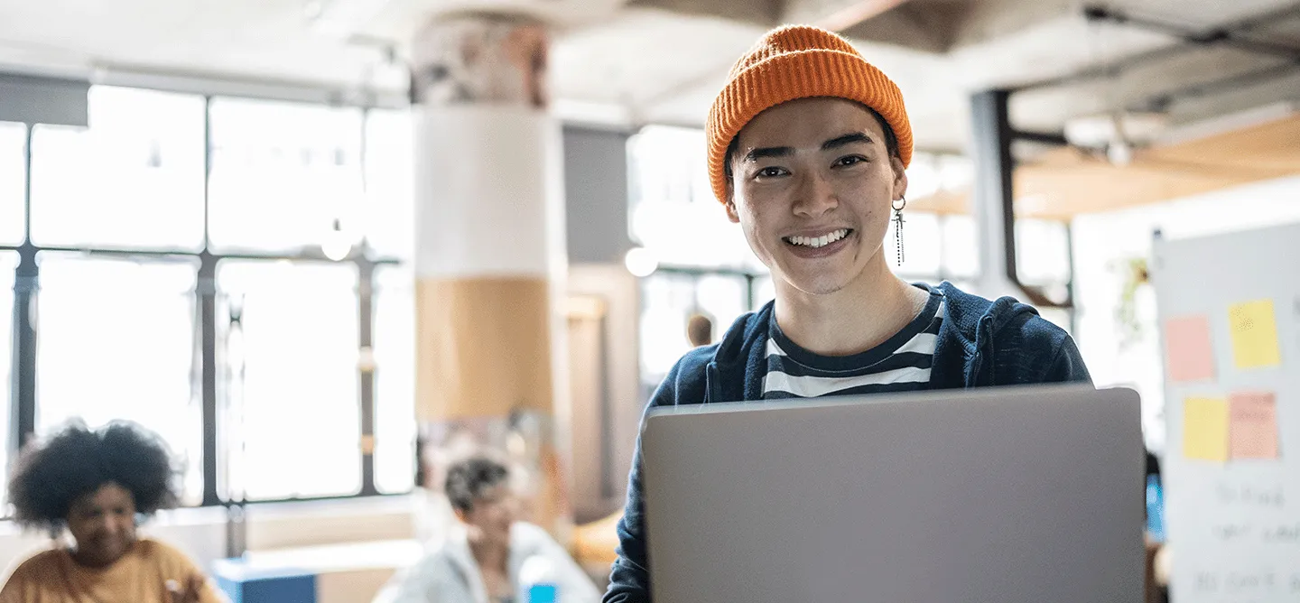 Praxispartner für ein duales Studium - ein Student schaut in die Kamera und sitzt vor seinem Laptop