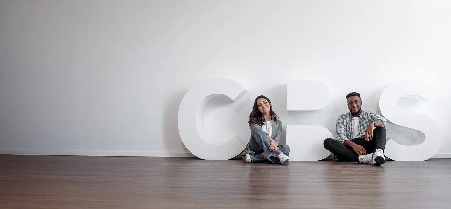2 Studierende auf dem Boden sitzend vor dem großen CBS Logo