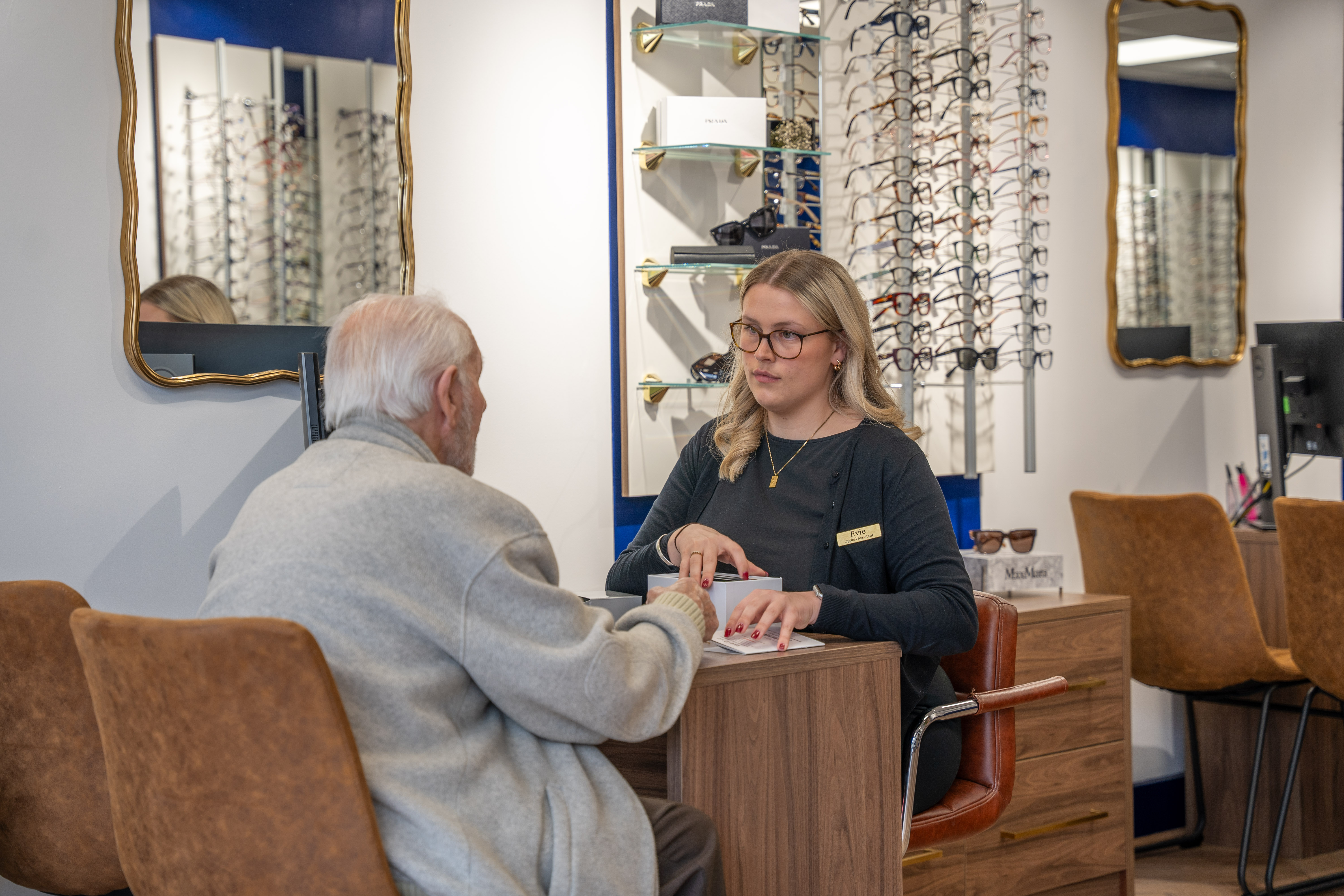 Optician helping elderly customer choose glasses in eyewear store