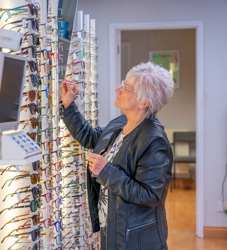 Older woman browsing colorful eyeglasses display in optical store