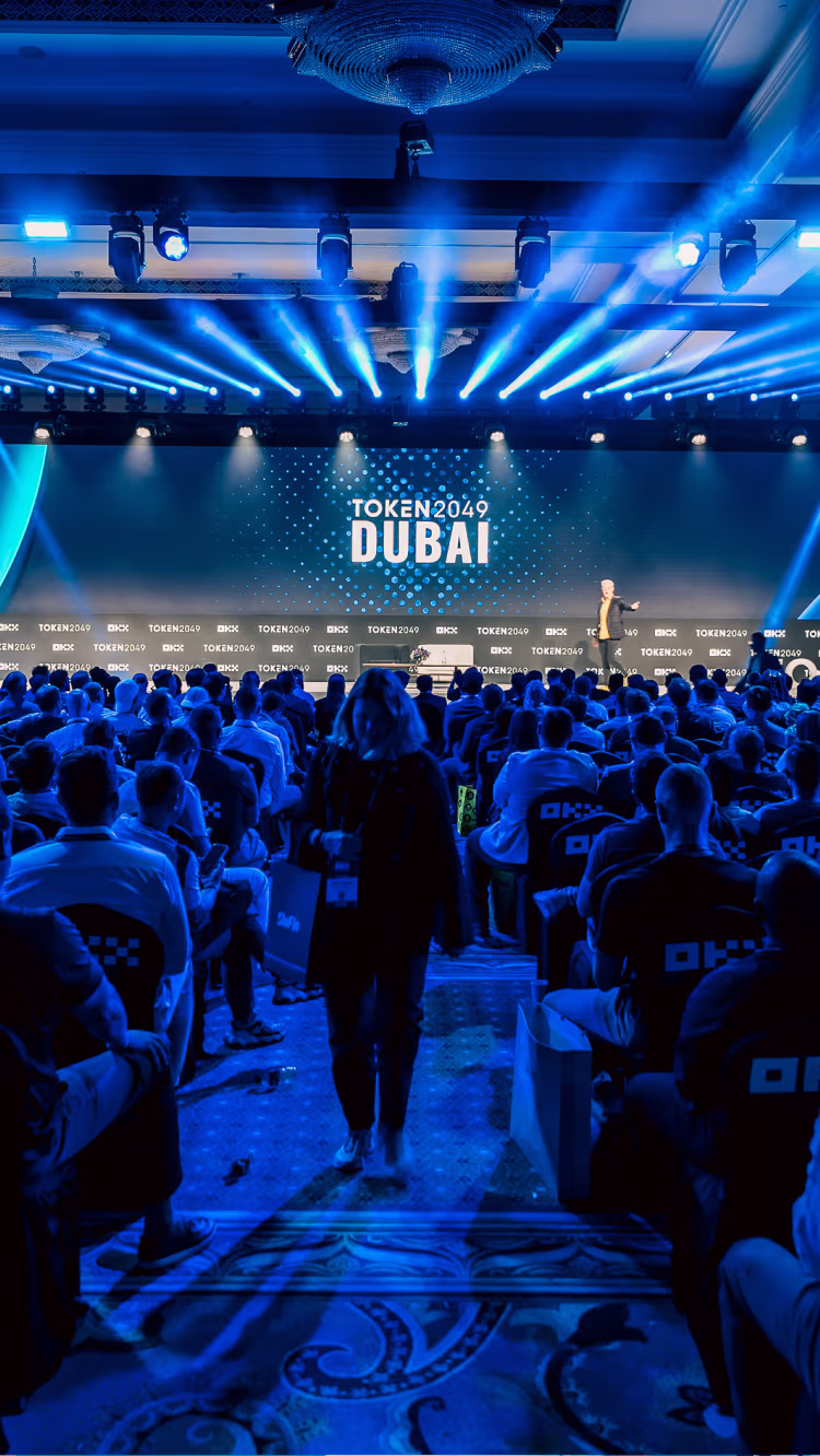 Audience watching a speaker on stage at the TOKEN2049 Dubai event under blue lighting.