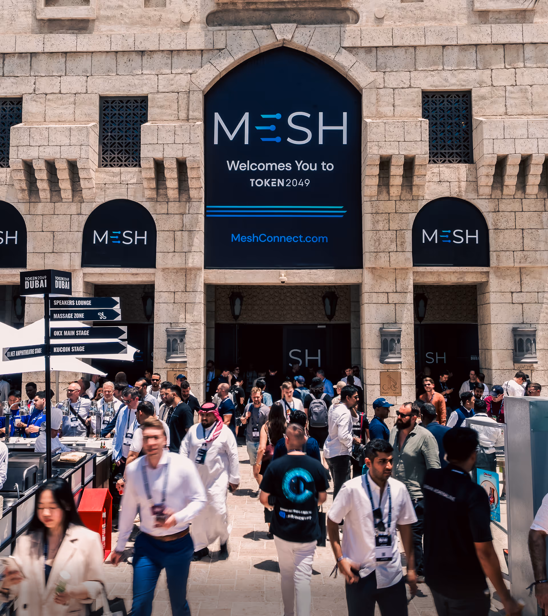 Crowd of people entering and mingling outside a stone building with Mesh signage welcoming attendees to Token 2049 in Dubai.