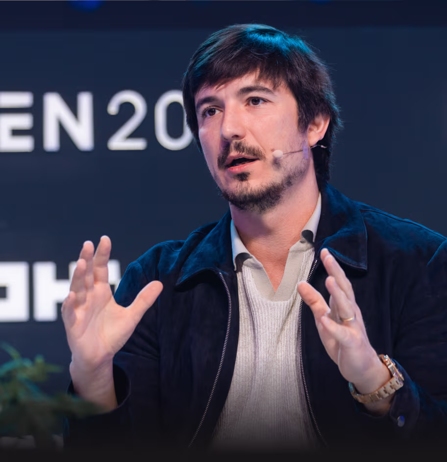 Man with microphone headset speaking and gesturing with hands during a presentation or panel discussion.