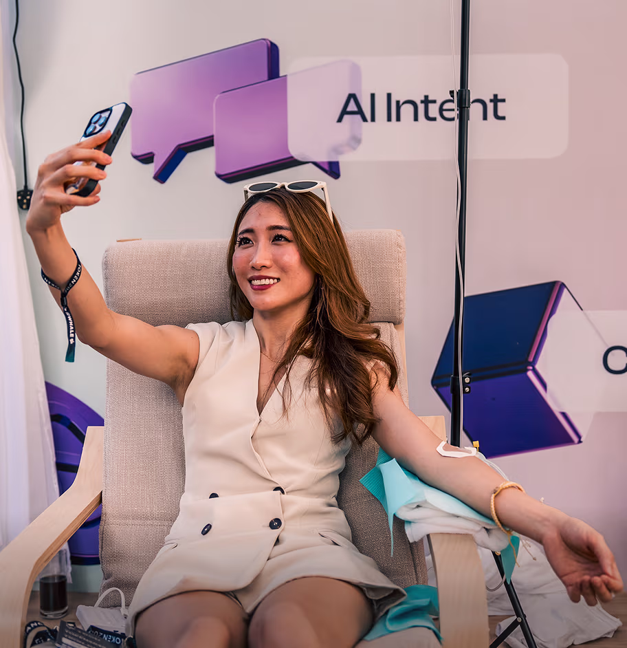 Young woman sitting in a chair, taking a selfie while donating blood with an IV in her arm.