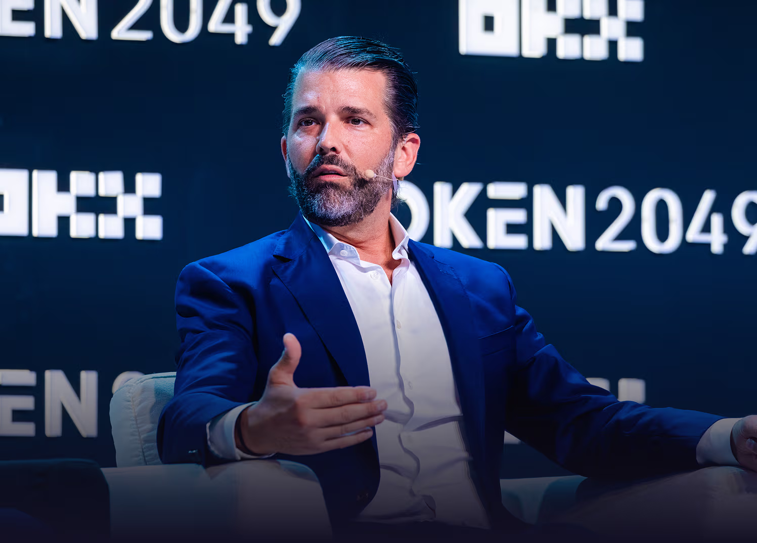 Trump Jr speaking with a hand gesture on stage in front of a backdrop reading TOKEN 2049.