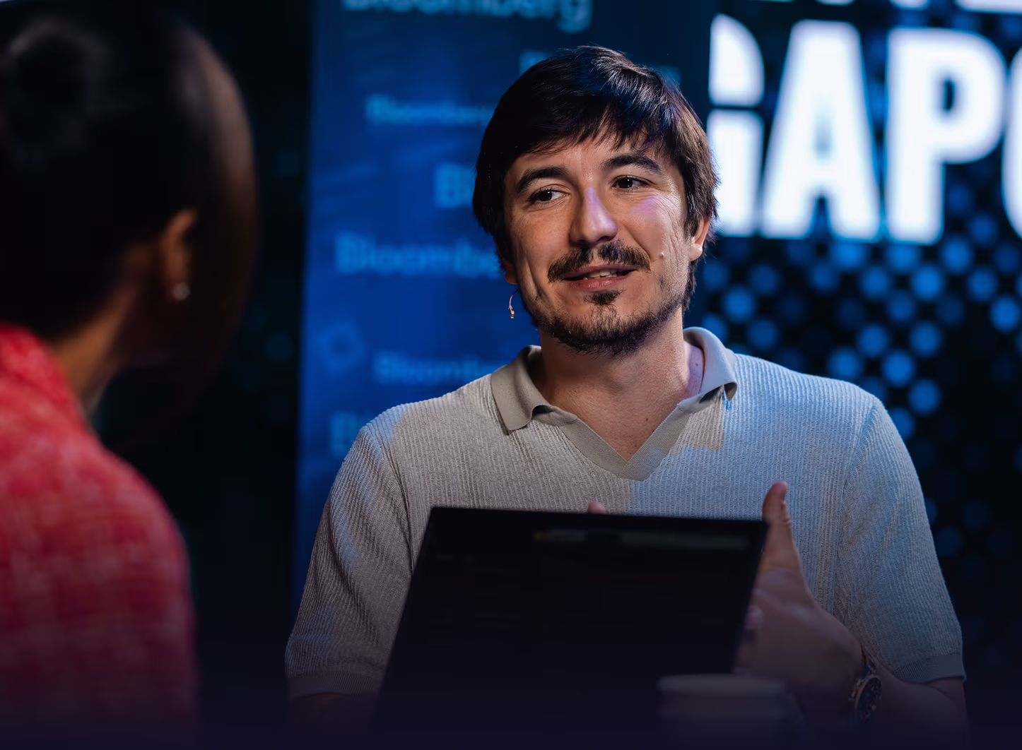 Vlad Tenev speaking during an interview with a woman in a red top.