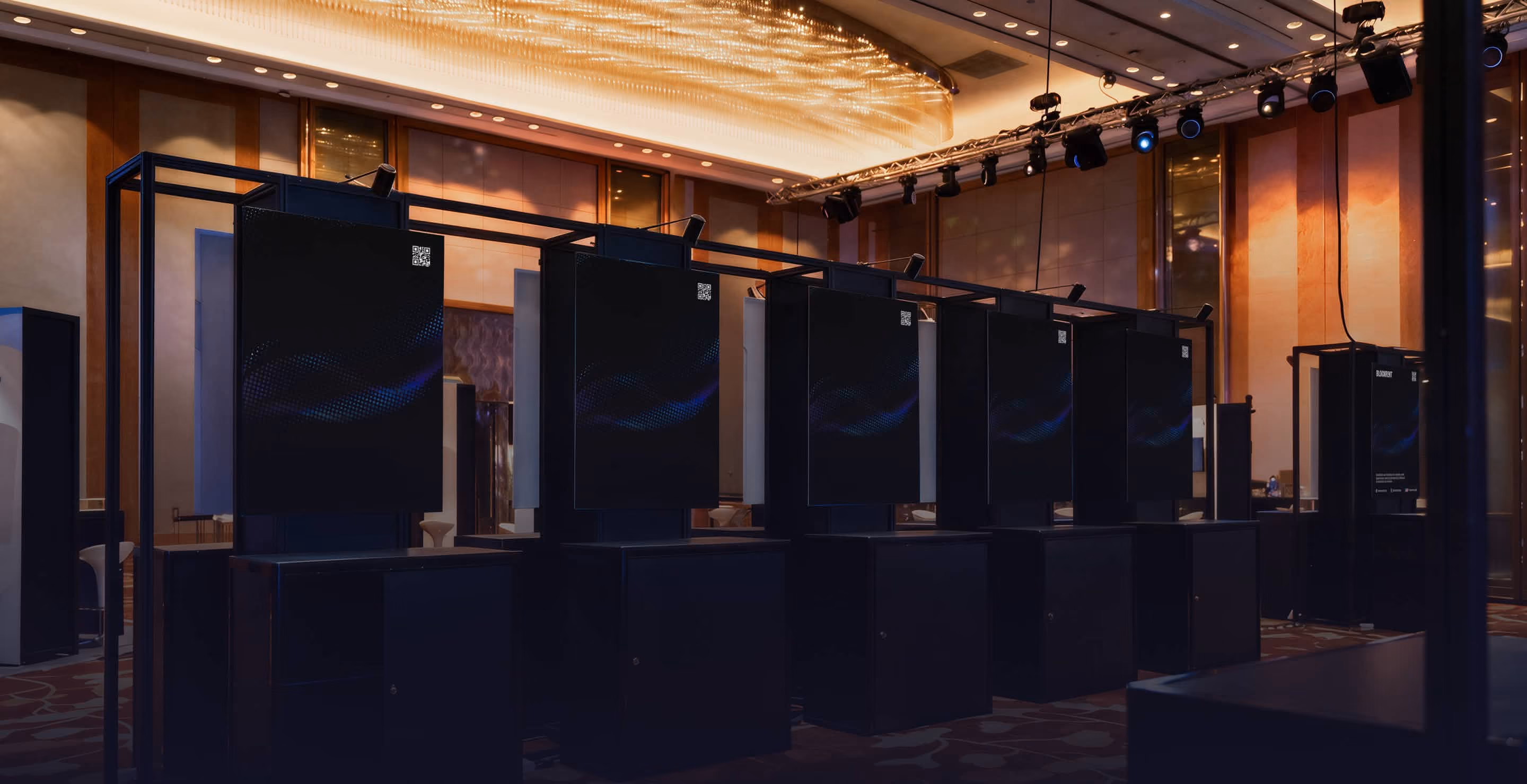 Empty modern booth setup with black display panels under a chandelier in a conference room.