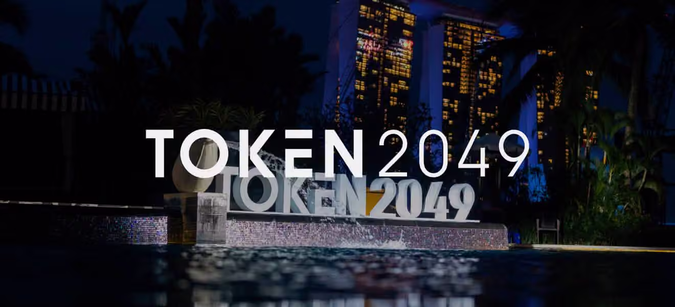 Large illuminated sculpture of the text 'TOKEN 2049' beside a pool at night with city lights in the background.