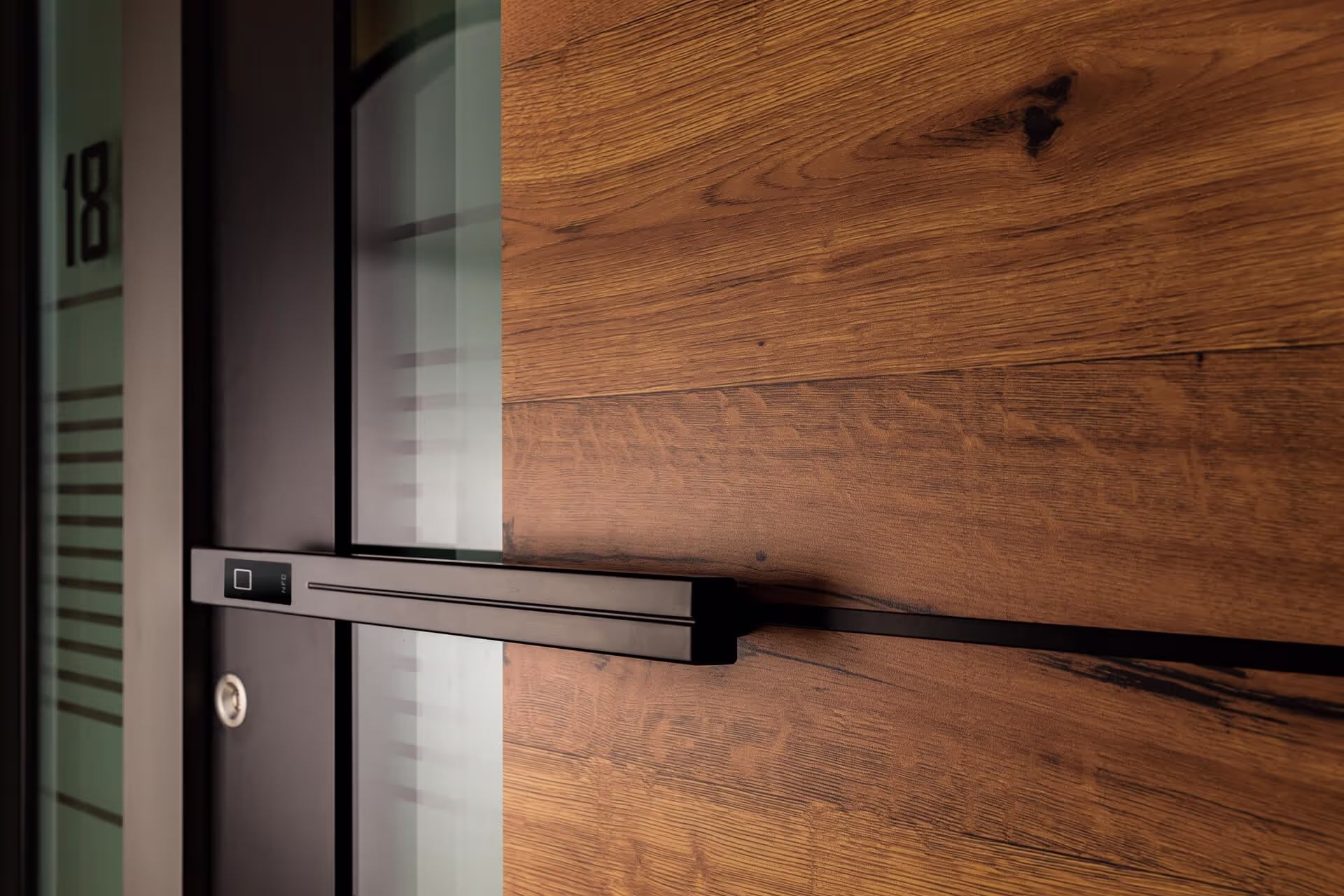 Moderner Türgriff aus schwarzem Metall an einer Holztür mit markanter Maserung und Glaseinsatz mit der Hausnummer 18.