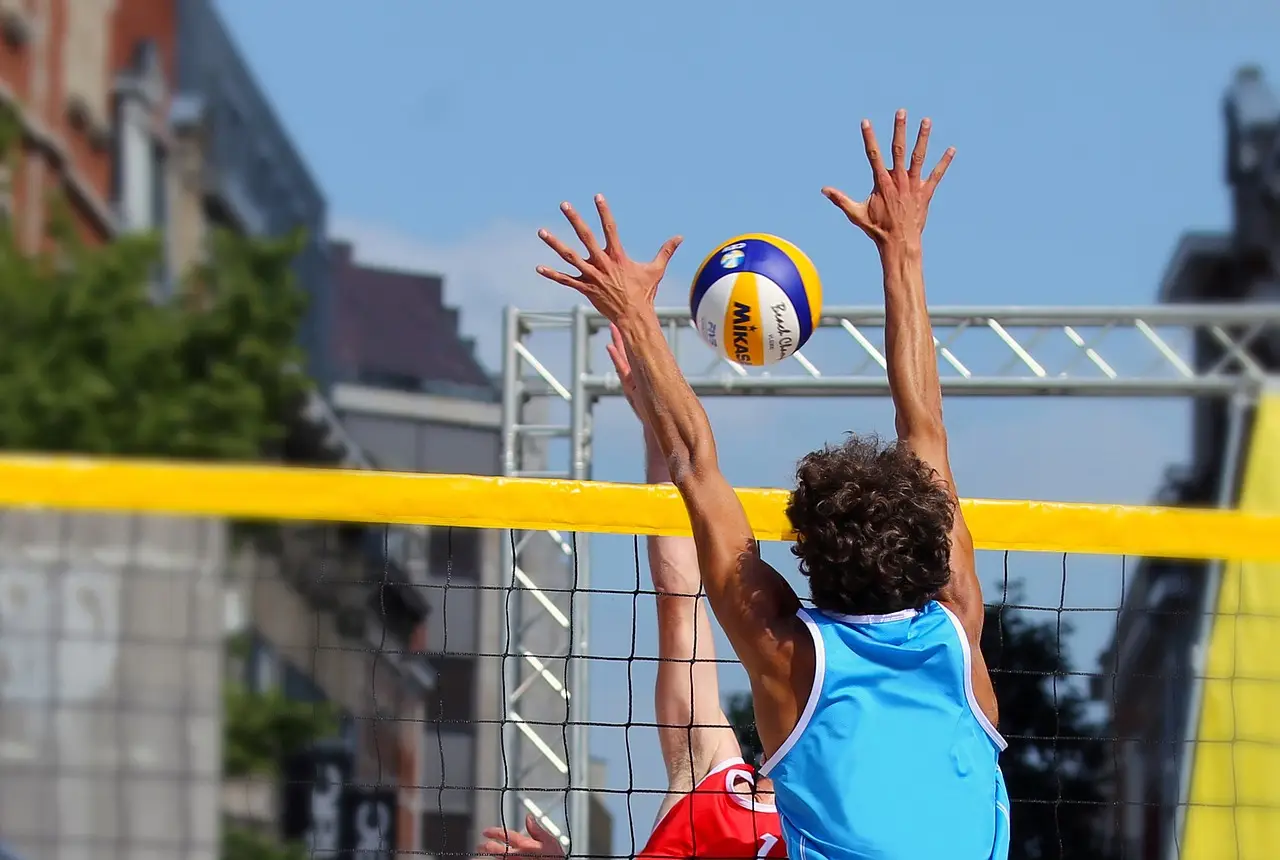 Deux joueurs de beach-volley sautant près du filet pour intercepter un ballon Mikasa bleu, jaune et blanc.